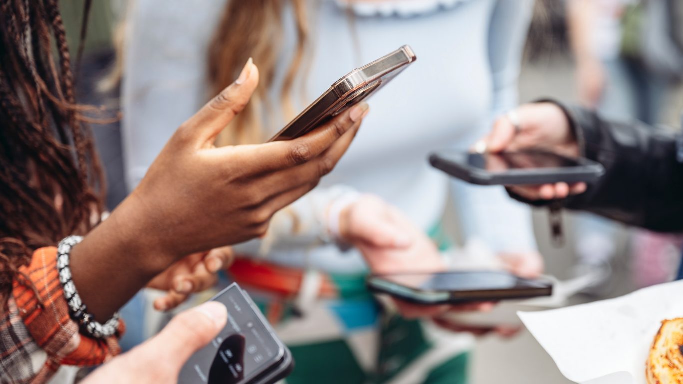 Several people standing together, each looking at their own phone.
